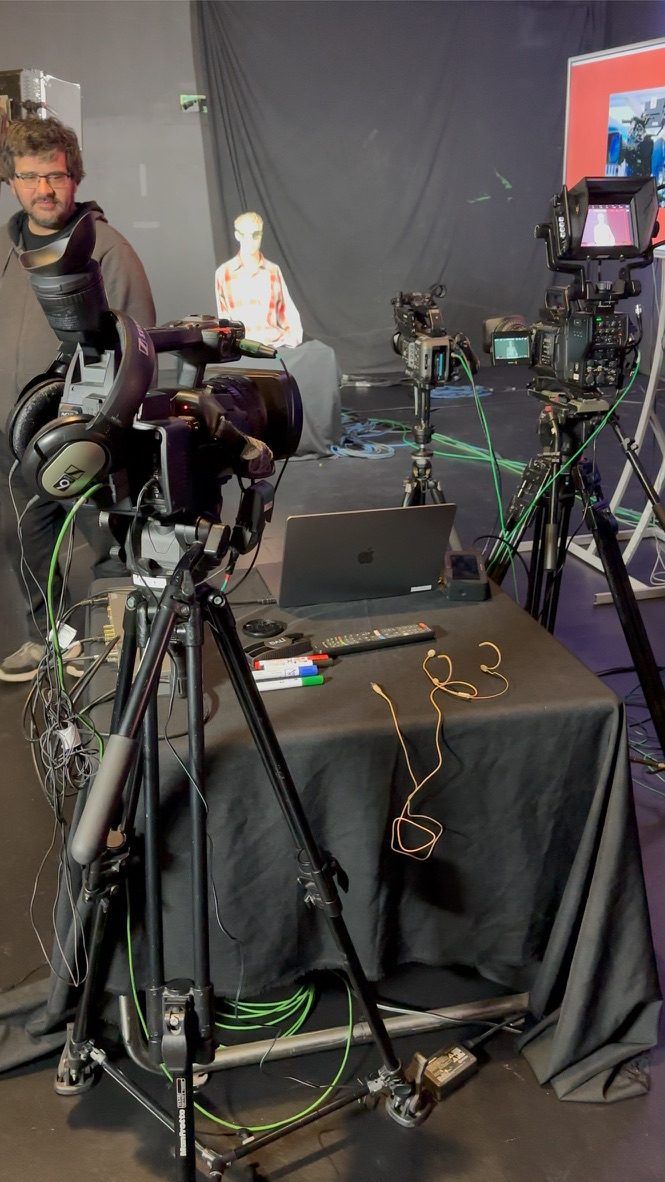 Cámara de estudio con trípode y monitor sobre una mesa con paño negro, en el set del taller.