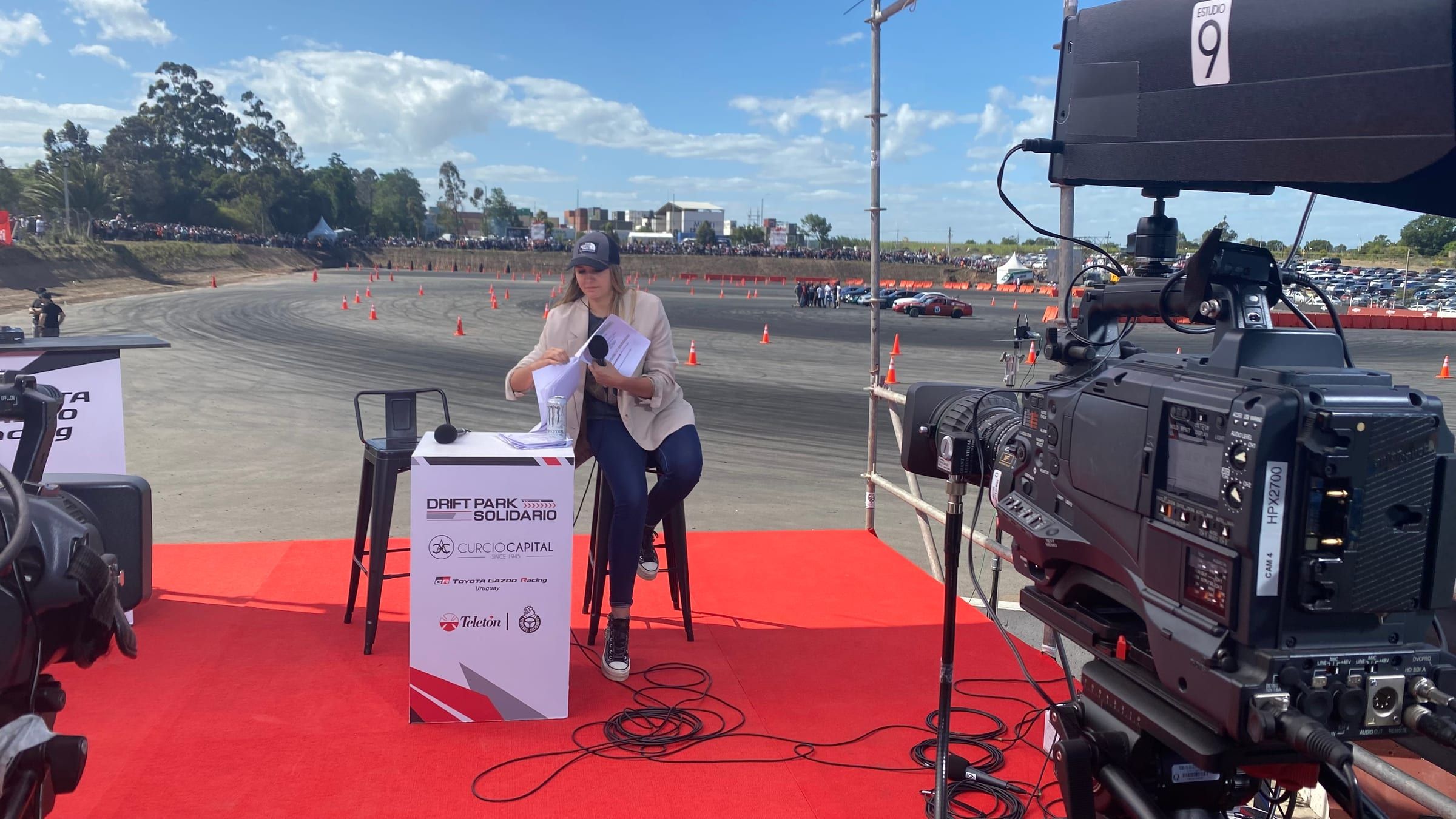 Presentadora sentada en el set del Drift Park Solidario de Toyota Gazoo Racing, junto a una cámara de Estudio9 y con la pista de drifting al fondo
