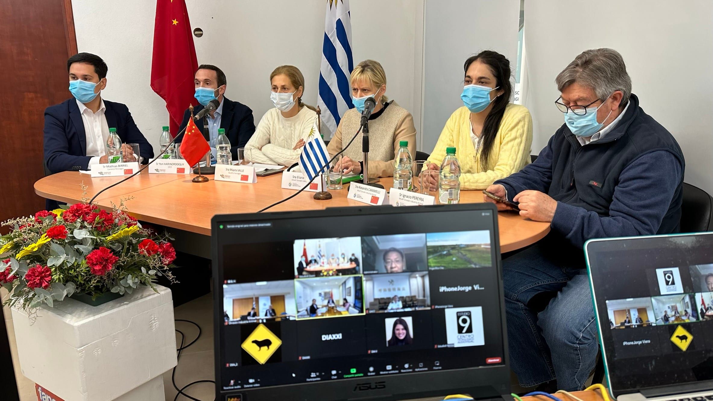 Delegaciones en una sala con cámara, notebooks y pantallas con la videollamada de la auditoría remota, entre las banderas de Uruguay y China.