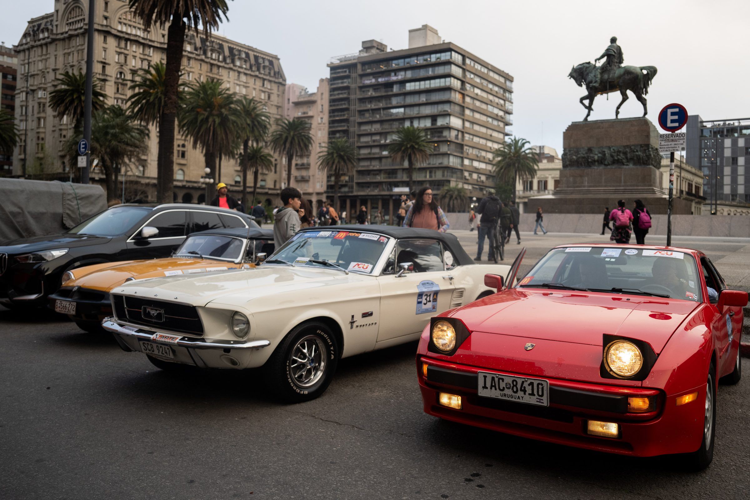 Autos deportivos clásicos estacionados frente a la Plaza Independencia antes de la largada, con la estatua de Artigas al fondo