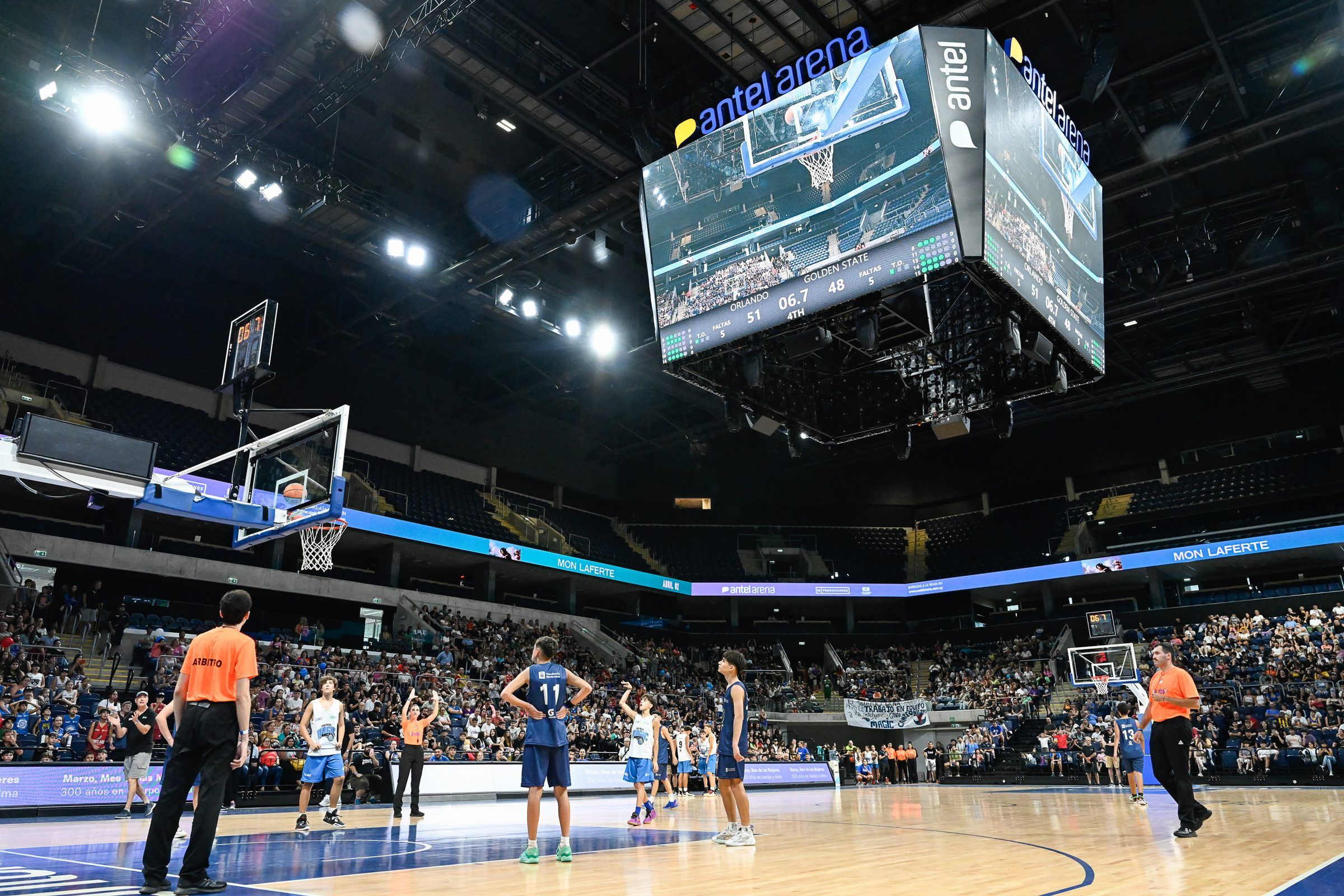 Cancha del Antel Arena durante un partido de las finales del torneo Jr. NBA, con el marcador colgante y el público en las gradas