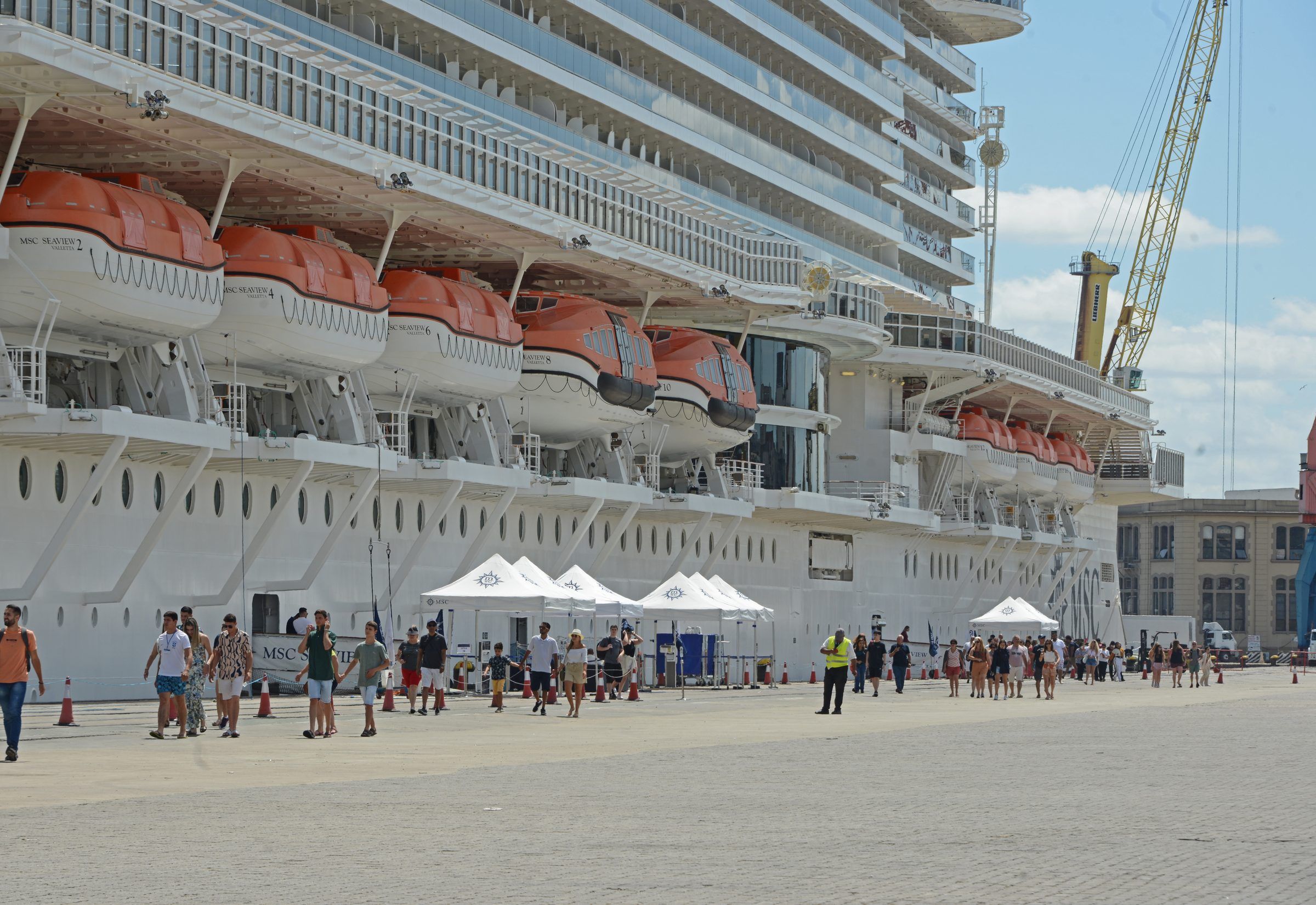 Costado del crucero atracado, con carpas de atención y turistas en el muelle del Puerto de Montevideo.