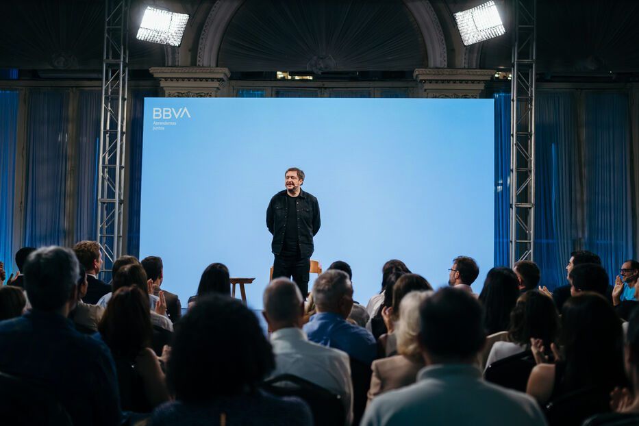 Hernán Casciari de pie en el escenario frente a la pantalla con el logo de BBVA y el público sentado, durante Aprendemos Juntos