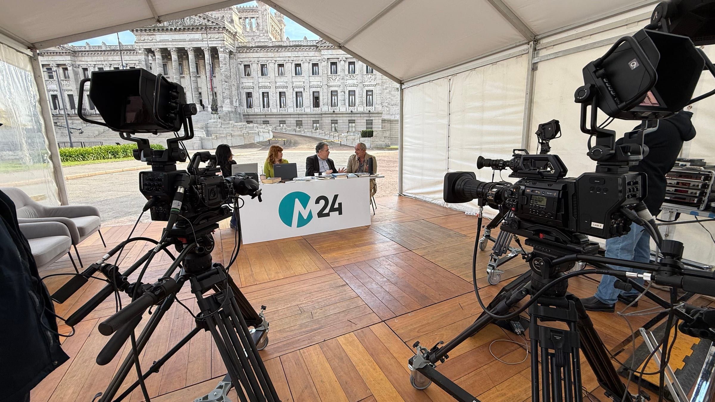 Dos cámaras de estudio sobre pedestal frente a la mesa de M24, en una carpa con vista al Palacio Legislativo