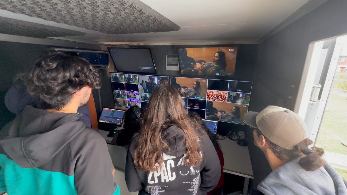 Estudiantes, vistos de espaldas, observan el control de realización del móvil con multipantalla y mezclador.