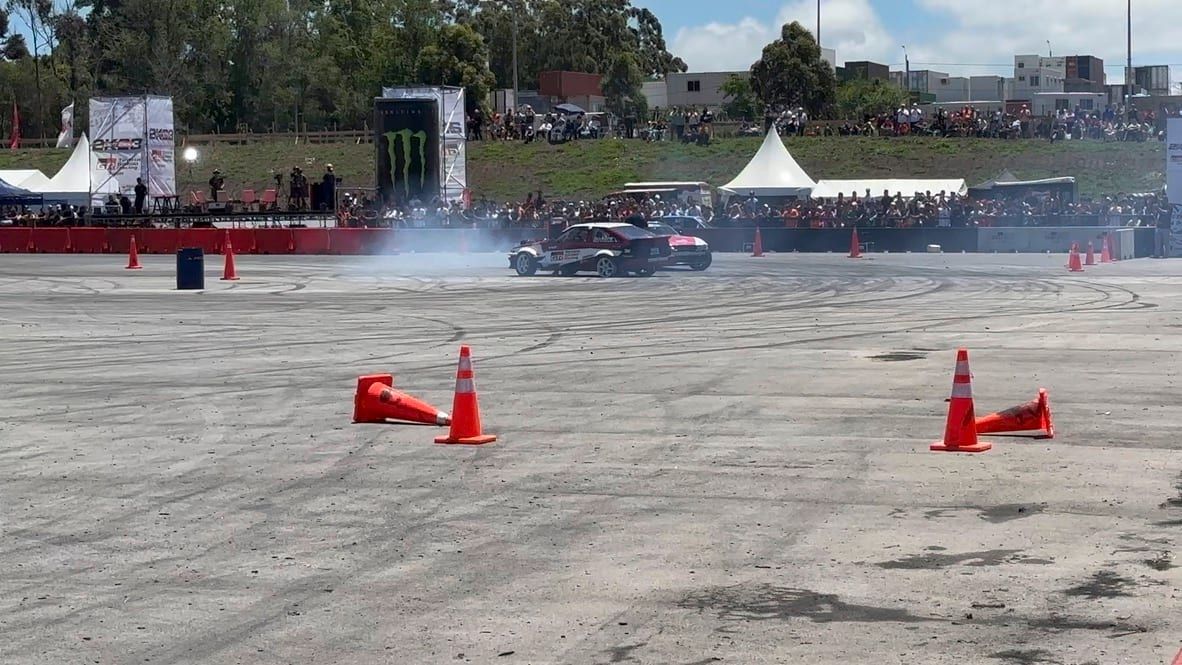 Auto de drifting levantando humo en la pista entre conos, con las tribunas llenas al fondo
