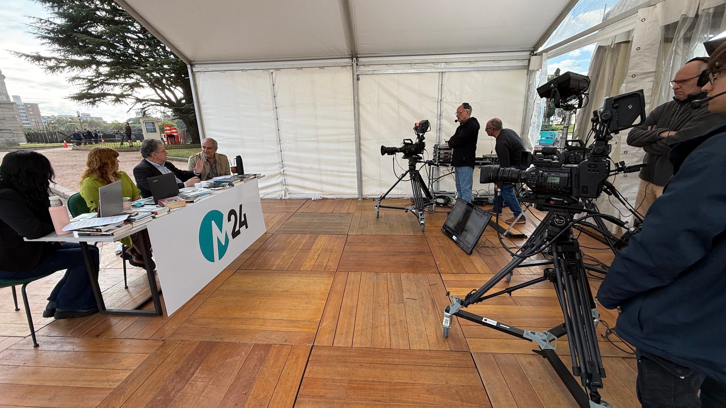 Carpa de la transmisión de M24 vista desde el costado, con cámaras y equipo técnico frente a la mesa