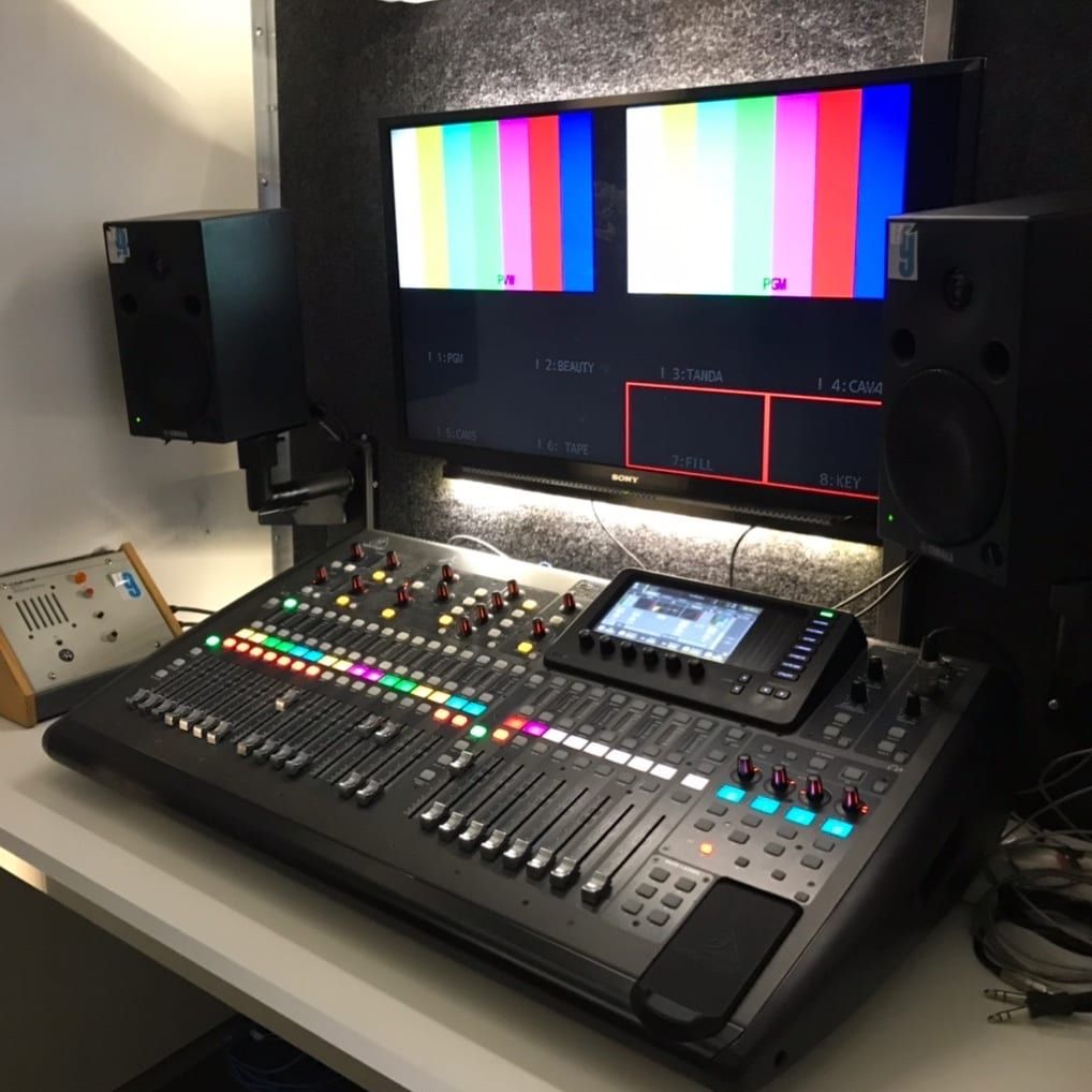 Cabina de audio del camión: consola digital frente a un monitor con barras de color y dos parlantes de estudio